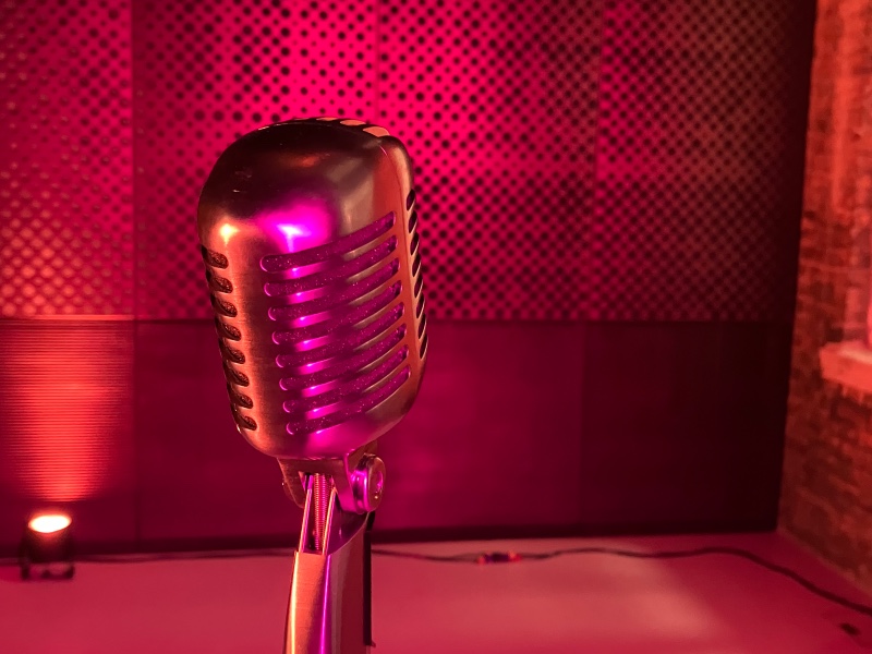 A silver 50's style microphone with and orange and pink flare is in the foreground with a pink textured background.