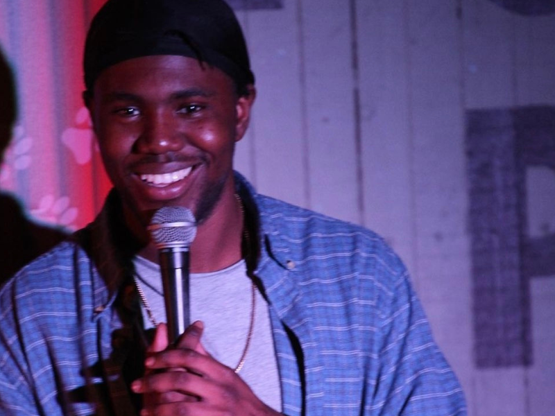 close up of a man with microphone smiling, purple and blue tones in the background