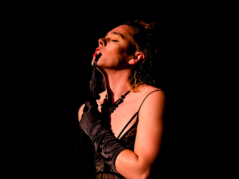 Neo-Burlesque performer taking there glove off in a seductive, sexy manner with their mouth.