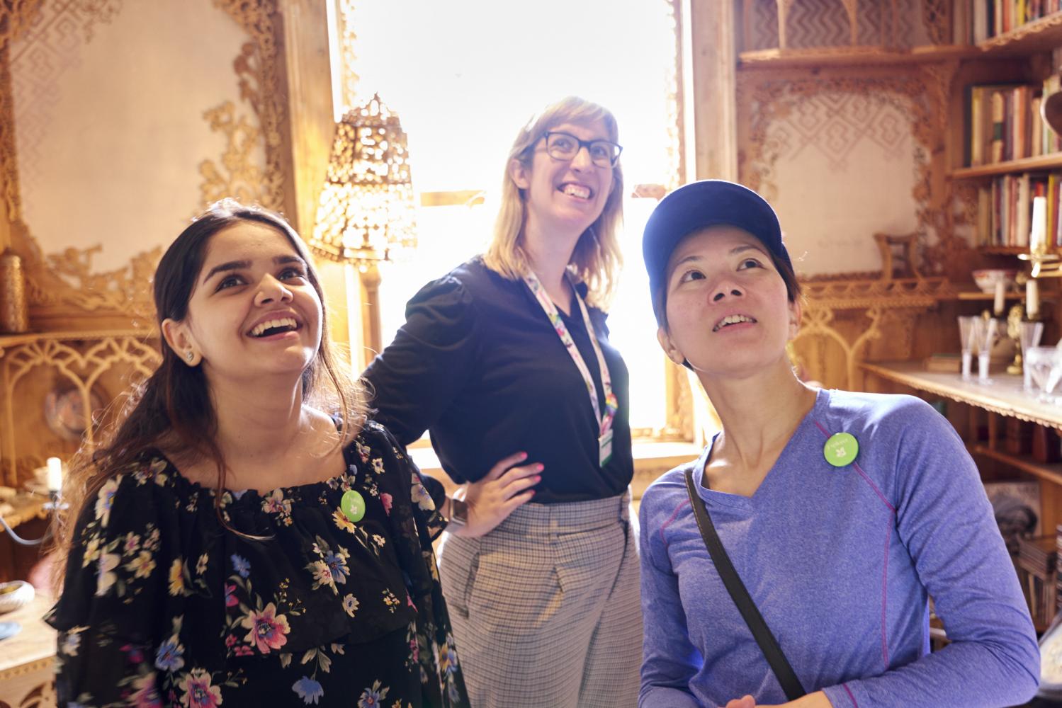 3 women standing in a wood carved interior looking up.