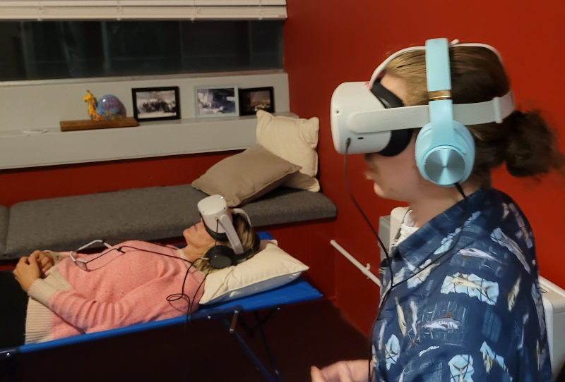 Man seated & Woman lying both with VR headsets & headphones